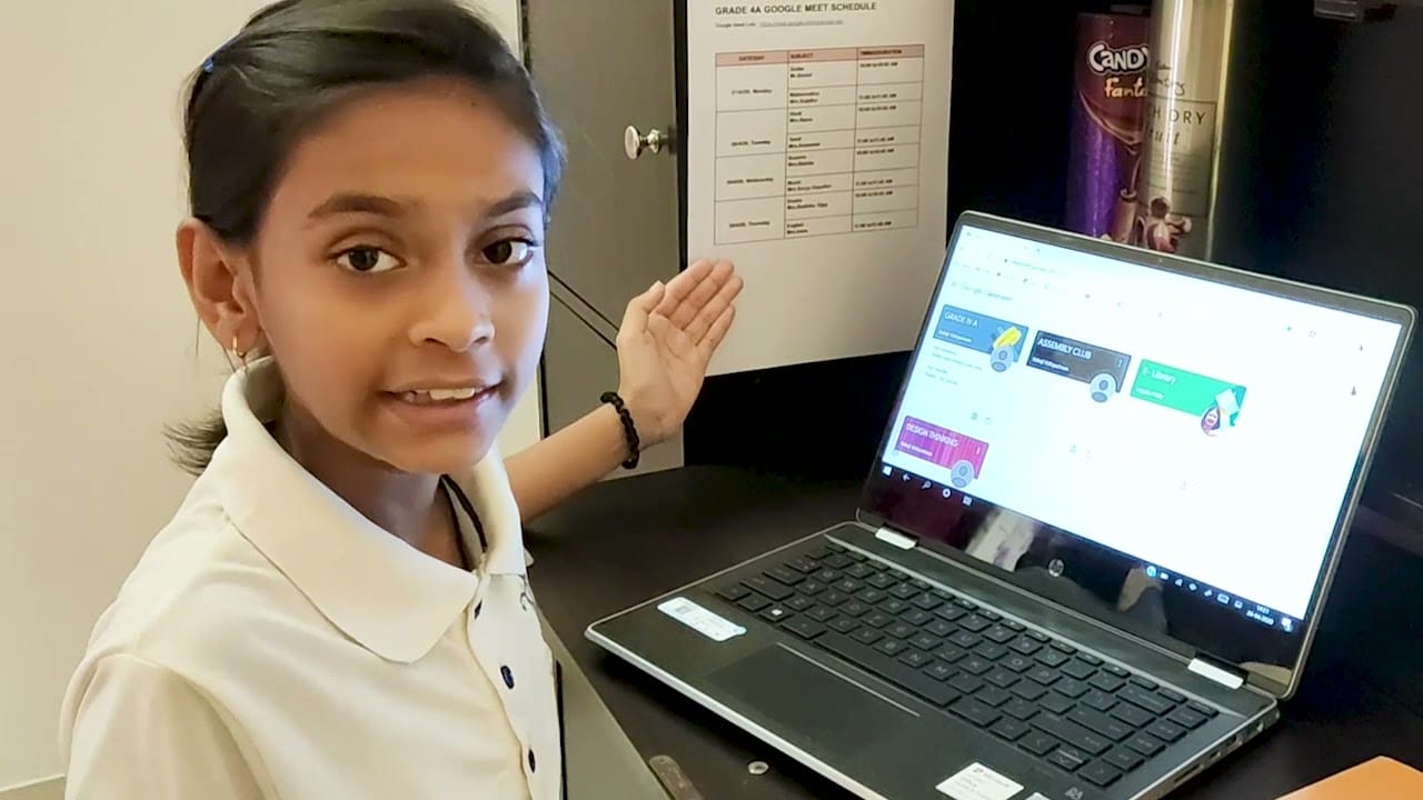 A young student pointing at a laptop screen while learning online at home.