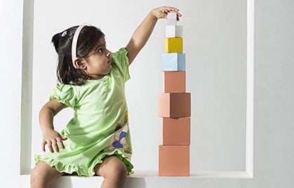 A girl child from Babaji Vidyashram's Nursery section stacking colourful Montessori blocks according to size.