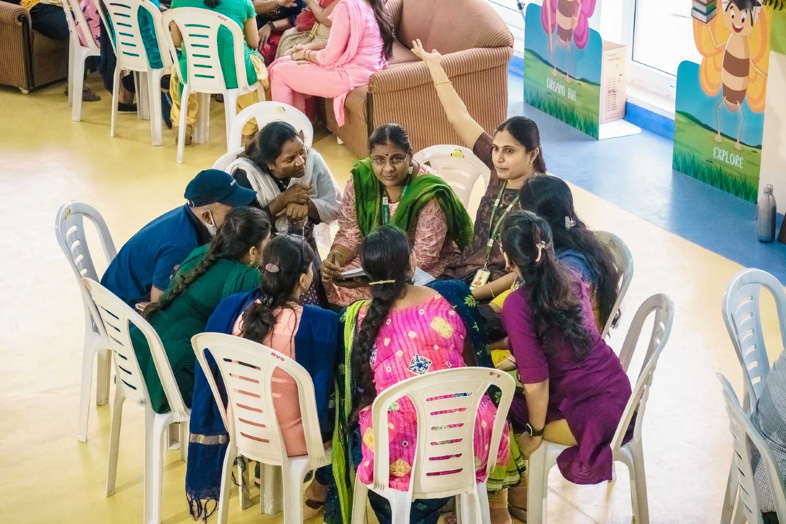 In a group discussion among teachers, one staff is pointing her hand somewhere and other are listening to her.